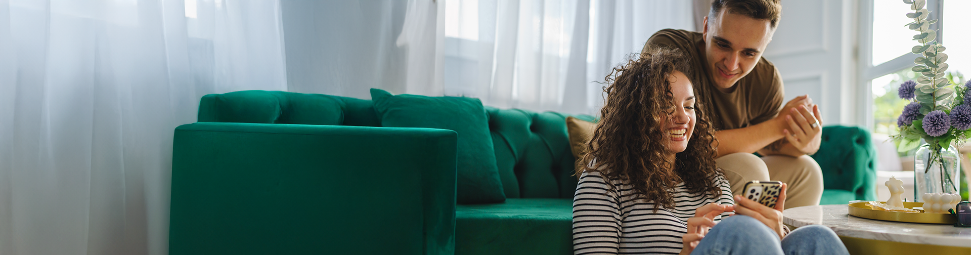 man sitting on a green couch behind a smiling woman who is sitting on the floor holding a phone