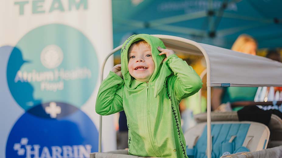 little boy of toddler age smiling and wearing a green hooded costume