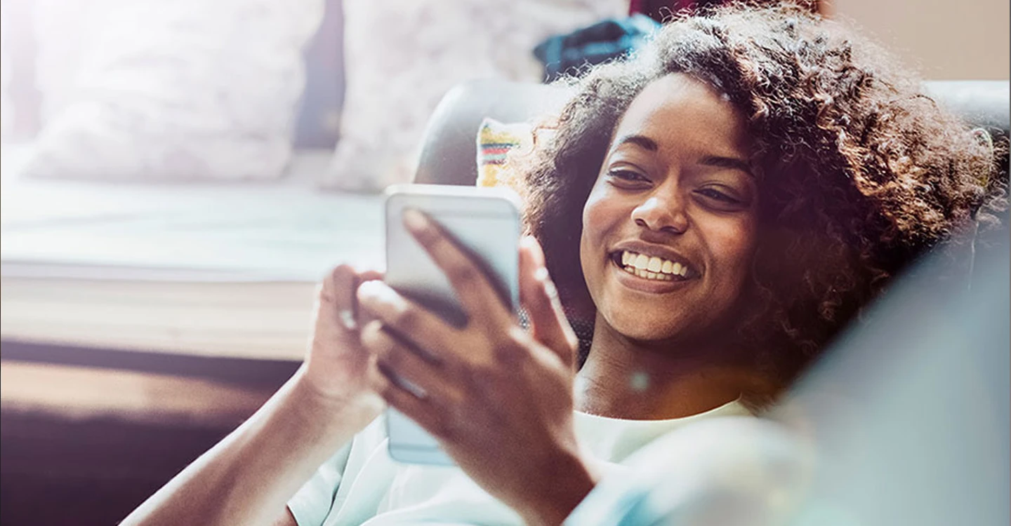 young woman lying on a couch and smiling while on her phone