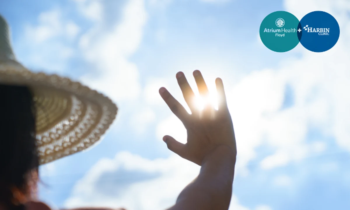 Person raising hand toward the sun while wearing a summer hat