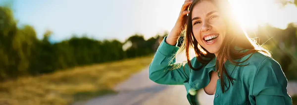 A woman stands outside in the sun with a road behind her. 