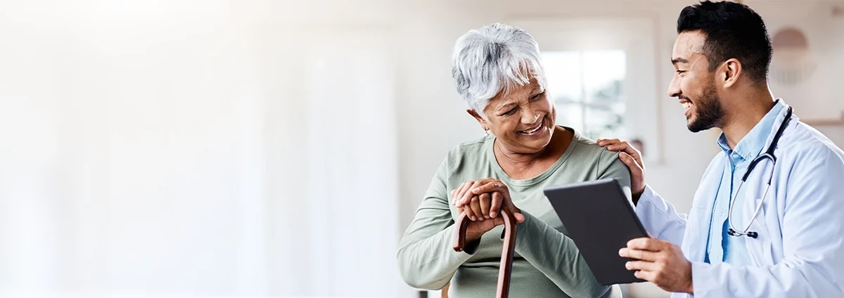 Alt text: A younger doctor talks with a senior patient while the doctor’s hand rests on the patient’s shoulder.
