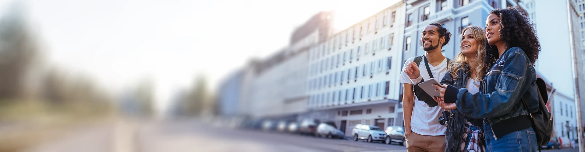 A man and two women look at a tablet in an outdoor city environment.