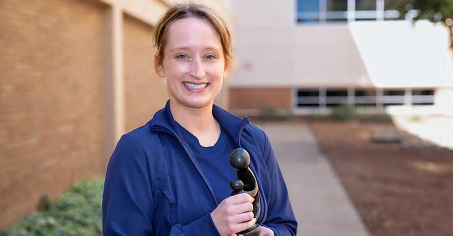 Caroline Pace standing outside and holding her DAISY Award sculpture
