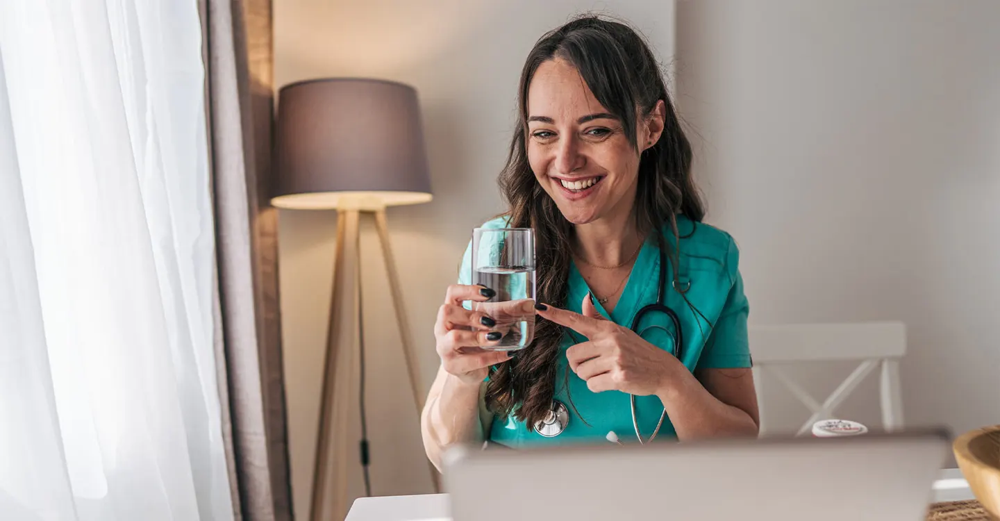 woman with dark hair and wearing scrubs holding a glass of water